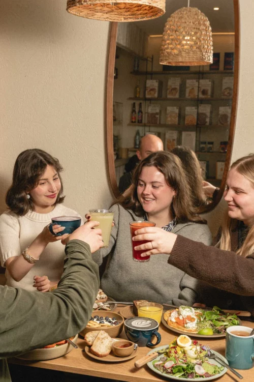 Quatre amies rient autour d'une table chez Marlette Abbesses, dégustant des boissons et des assiettes gourmandes faites maison