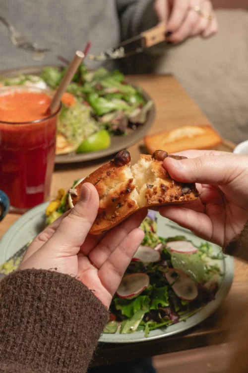Hand holding a generous organic pastry with chocolate chips, plate of fresh salad and red juice at Marlette Abbesses