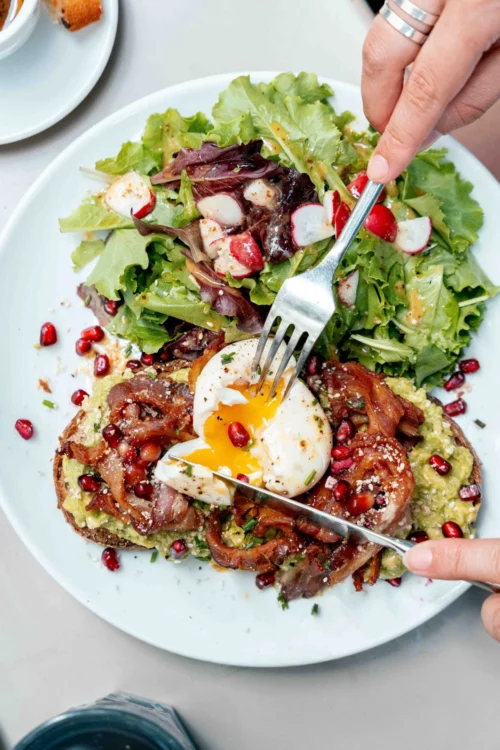 Gourmet brunch plate with crispy avocado toast, runny fried egg and fresh salad at Marlette