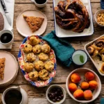 Assortiment gourmand de pâtisseries bio faites maison et café Marlette : gâteau au chocolat, muffins, pain aux raisins, fruits frais sur table en bois