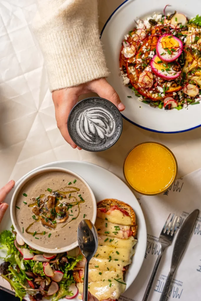 Tasse de café avec latte art tenu à la main, accompagnée d'assiettes de brunch gourmand chez Marlette