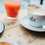 Tasse de café Marlette avec latte art, jus frais et viennoiserie sur table en bois