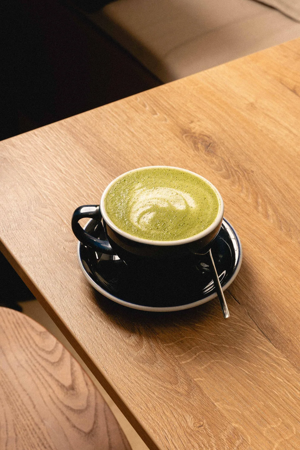 Taza negra de matcha latte gourmand con latte art, sobre mesa de madera cálida en Marlette