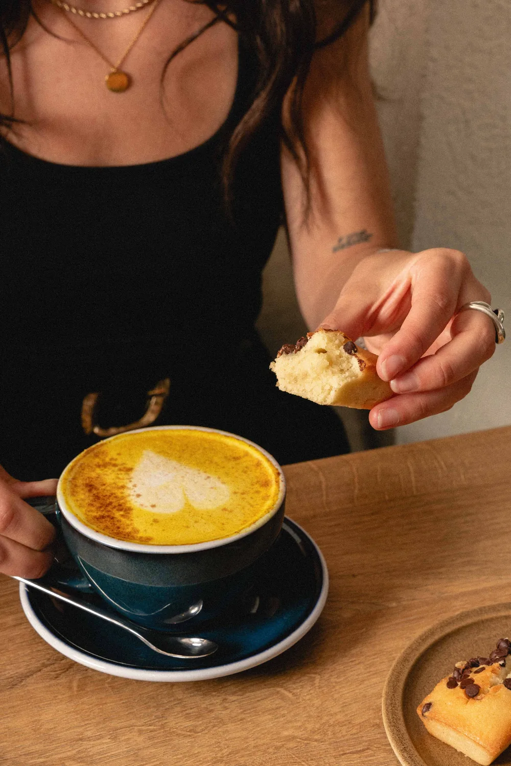 Mujer saboreando un turmeric latte dorado acompañado de una pastelería recién preparada en Marlette