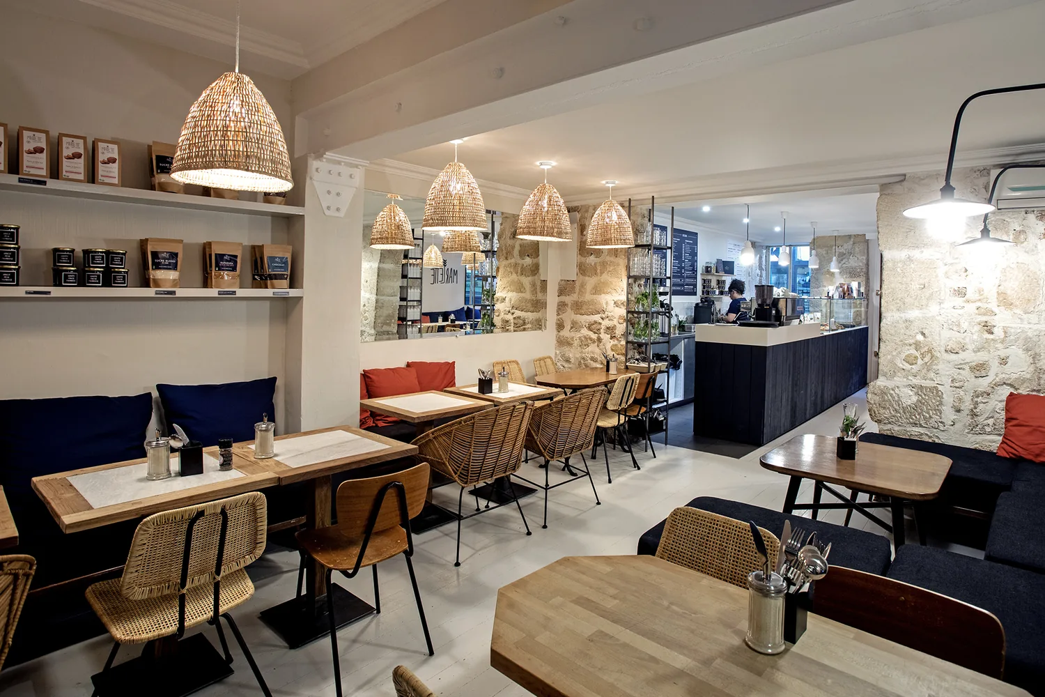 Interno accogliente del coffee shop Marlette con lampade in rattan, tavoli in legno e divani blu navy