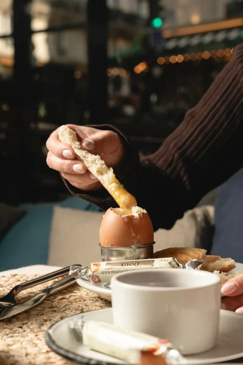 Main tenant un doigt de pain grillé au-dessus d'un oeuf à la coque lors d'un petit-déjeuner gourmand à Marlette