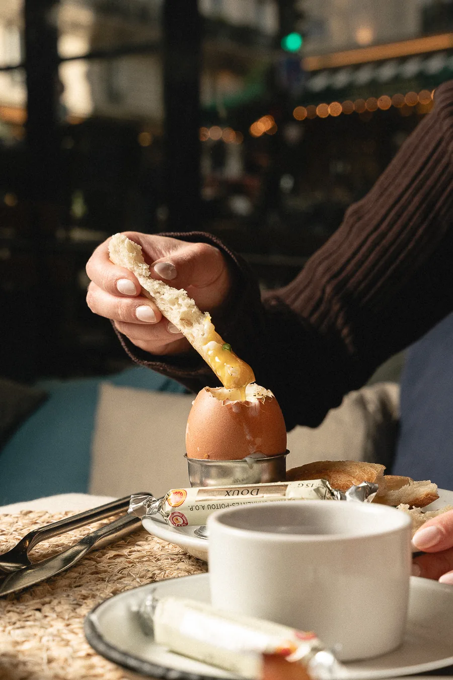Hand holding a finger of toast over a soft-boiled egg during a generous breakfast at Marlette