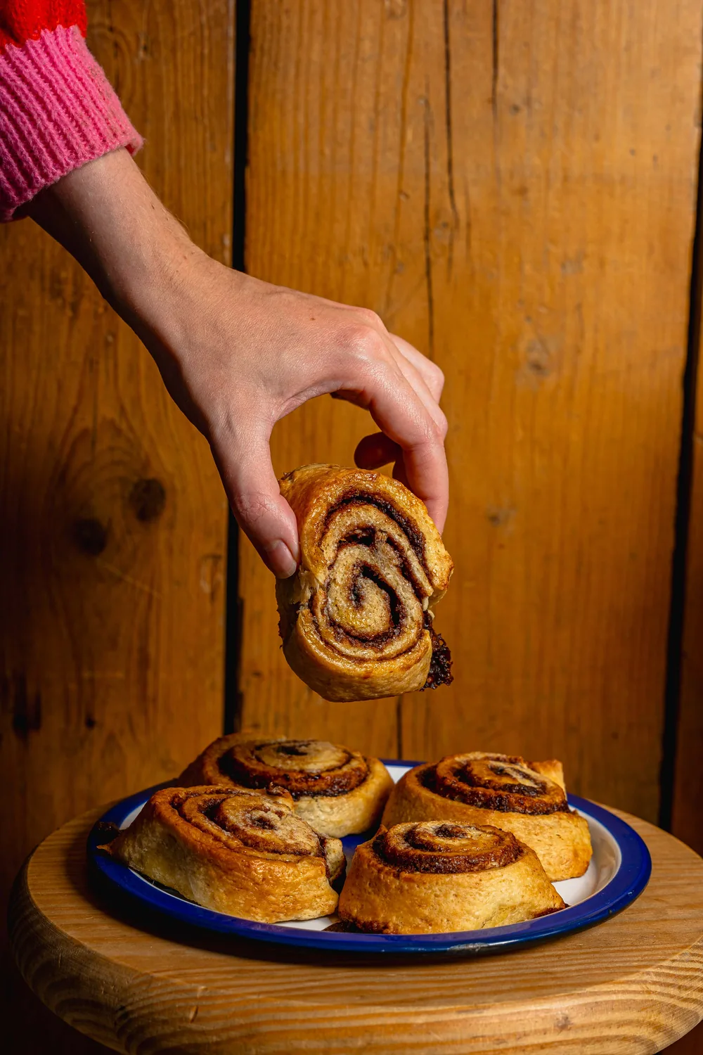Main qui attrape un pain au chocolat bio fait maison chez Marlette, assiette de pâtisseries fraîches sur table en bois