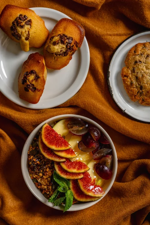 Assiettes blanches avec pâtisseries bio faites maison : madeleines aux pépites de chocolat et bowl gourmand aux figues fraîches