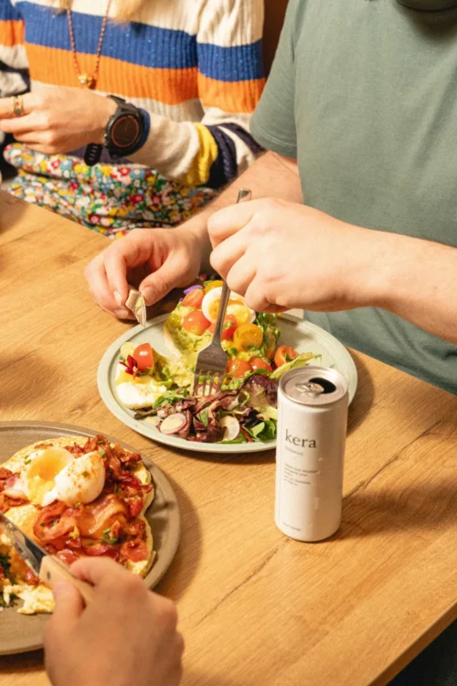 Two people sharing a Marlette brunch with fresh salad, tomato toast and drinks, convivial atmosphere around a wooden table