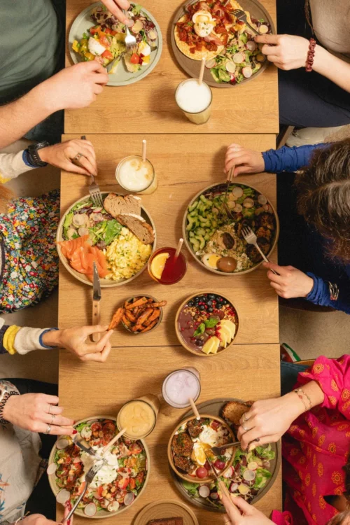 Aerial view of a shared brunch table with multiple diners, colorful plates and drinks, convivial Marlette atmosphere