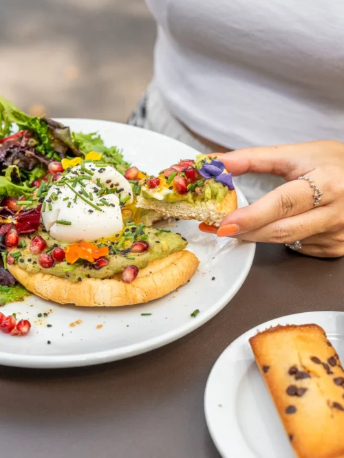 Client dégustant un avocado toast garni d'œuf poché et fleurs comestibles au coffee shop Marlette des Martyrs, Pigalle