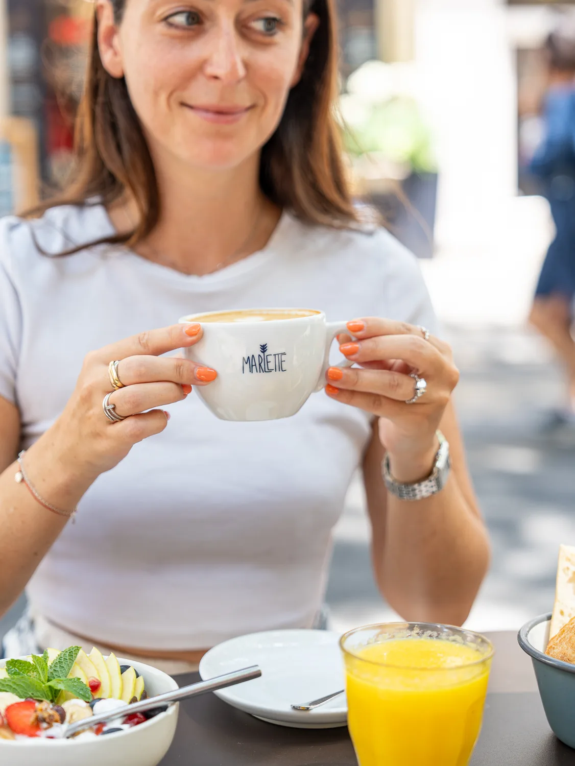 Une barista souriante tient une tasse de cappuccino Marlette avec latte art, devant son brunch au coffee shop des Martyrs à Pigalle.