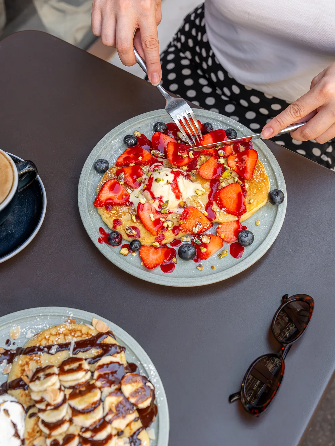 Cliente dégustant des pancakes garnis de fraises fraîches et myrtilles chez Marlette aux Abbesses, Montmartre, avec café à proximité