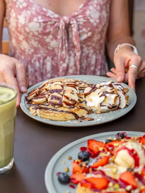 Cliente tenant une assiette de pancakes garnis de Nutella et banane, au coffee shop Marlette des Abbesses à Montmartre