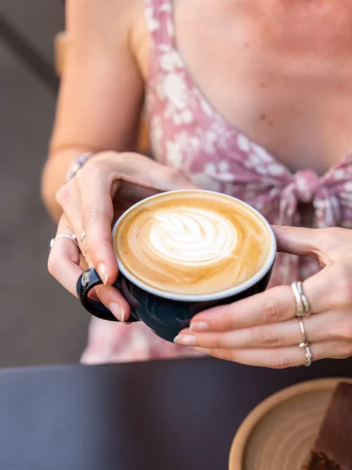 Cliente tenant un cappuccino avec latte art en forme de feuille au coffee shop Marlette des Abbesses, Montmartre