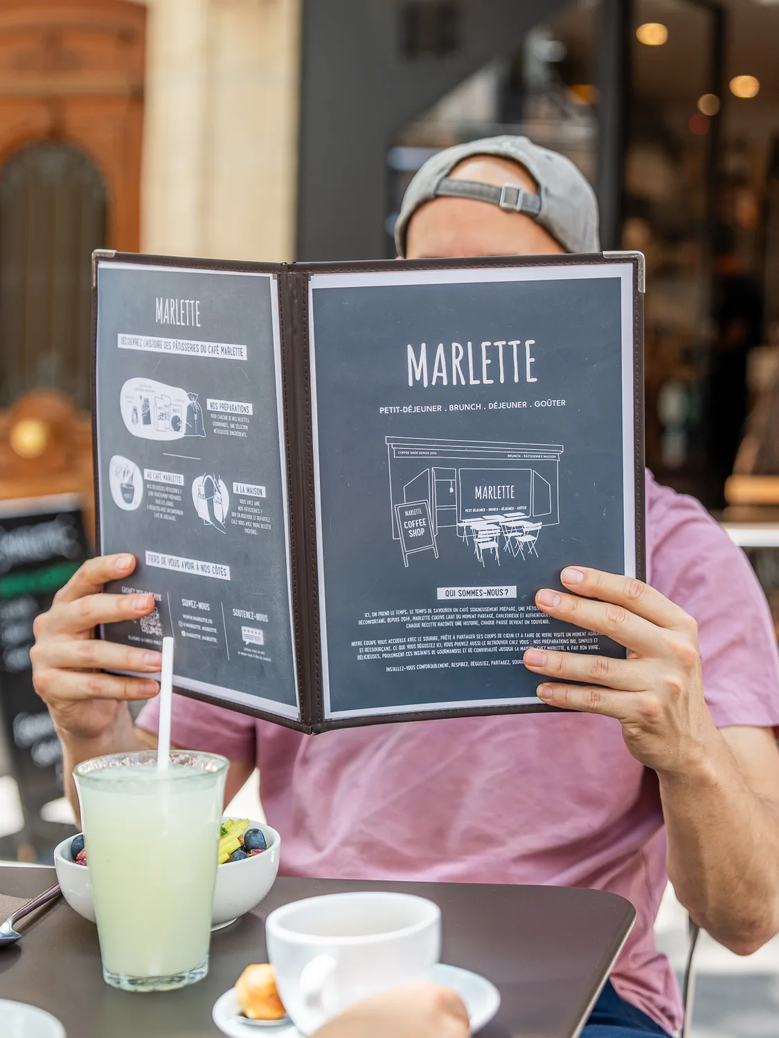 Cliente consulte le menu ouvert de Marlette devant son verre de boisson fraîche, coffee shop Martyrs Pigalle Paris