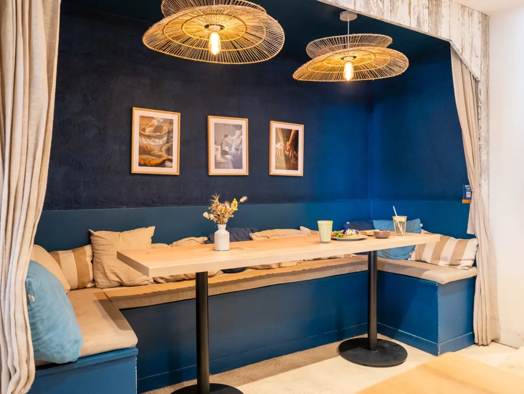 Alcôve de brunch avec banquette bleue, table en bois naturel et luminaires dorés, chez Marlette aux Abbesses à Montmartre