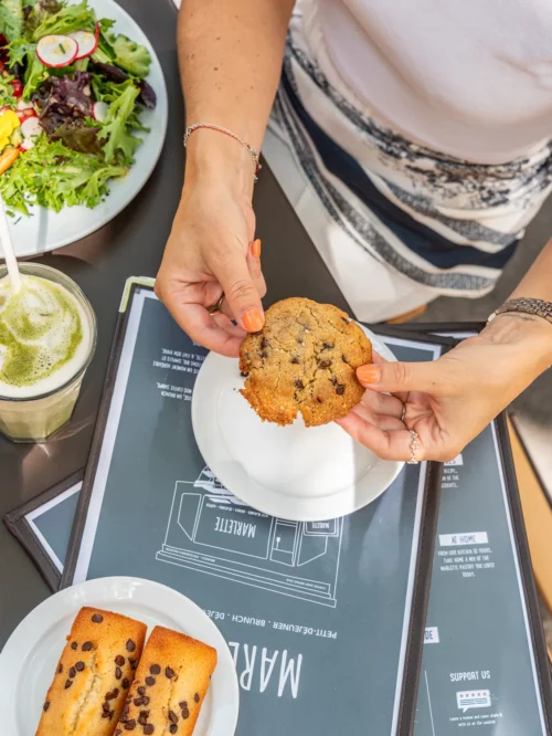 Cliente dégustant un cookie maison aux pépites de chocolat au coffee shop Marlette des Martyrs, à Pigalle, avec salade et boisson.