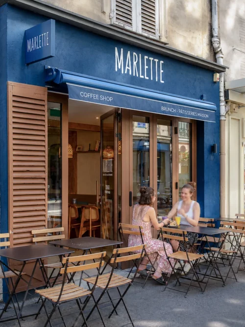 Devanture bleue du coffee shop Marlette avec terrasse extérieure, deux clients assis à une table, Montmartre Abbesses