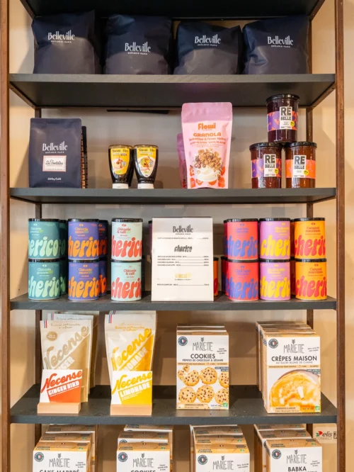 Présentoir en bois avec étagères exposant des boîtes de café Belleville, granola Floudi, confitures, cookies maison et crêpes Marlette au coffee shop des Martyrs à Pigalle