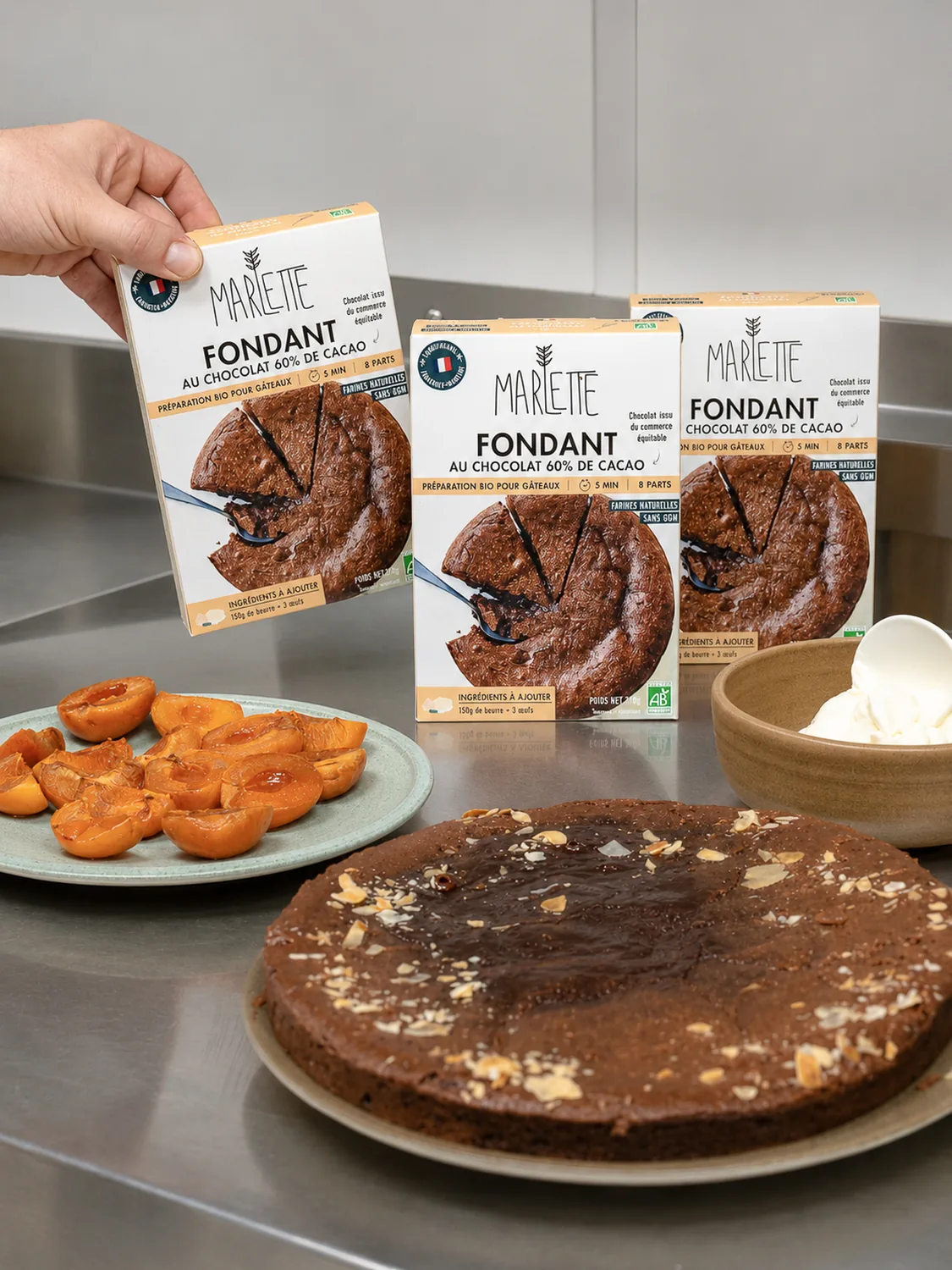 Mains tenant un paquet Marlette de fondant au chocolat bio 60% cacao, avec gâteau et viennoiseries sur table, Montmartre