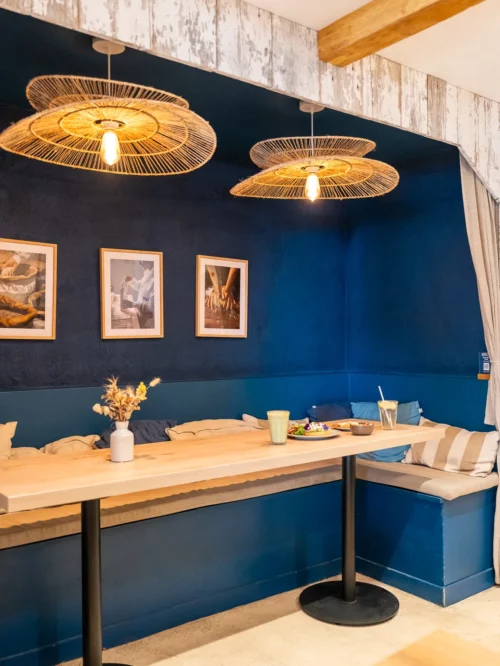 Banquette bleue élégante avec table en bois clair, luminaires en rotin doré et décoration murale au coffee shop Marlette à Montmartre
