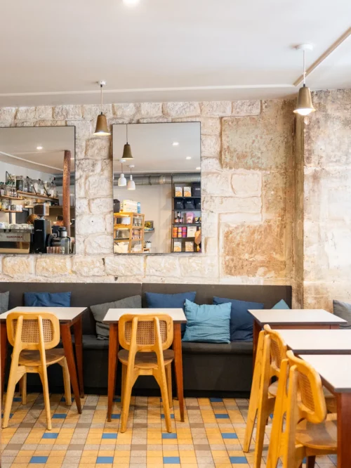 Intérieur chaleureux du café Marlette aux Martyrs à Pigalle, avec banquette grise, chaises jaunes et murs en pierre brute.