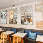 Intérieur du coffee shop Marlette aux Martyrs à Pigalle, avec banquette grise, chaises jaunes, murs en pierre, miroirs et luminaires en laiton