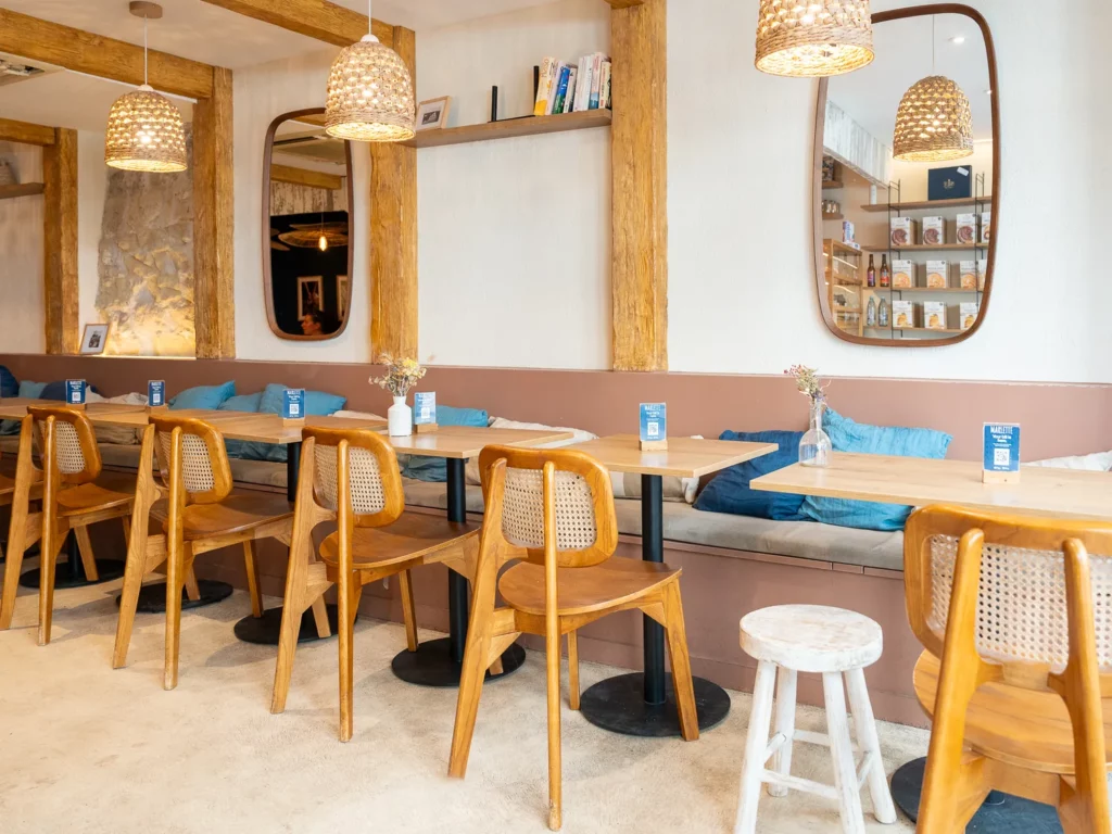 Intérieur chaleureux du coffee shop Marlette à Montmartre, avec chaises en bois, tables claires, banquettes bleues et luminaires design.