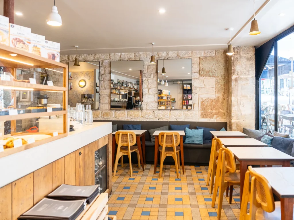 Intérieur chaleureux du coffee shop Marlette rue des Martyrs à Pigalle, avec comptoir en bois, tabourets jaunes et tables hautes.