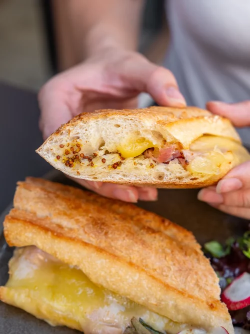 Mains tenant un sandwich au jambon et œuf sur pain grillé, plat de brunch signature chez Marlette à Montmartre