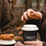 Deux mains tenant des cafés Marlette et des pâtisseries bio fraîchement faites, dans les rues de Montmartre