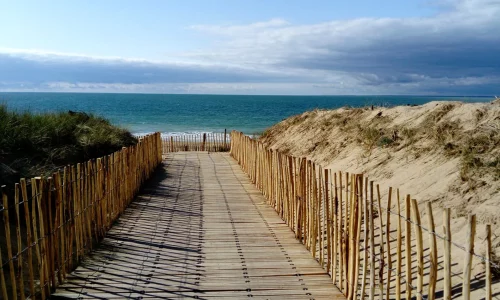 Chemin en bois traversant les dunes de l'Île de Ré face à la mer turquoise, inspirant les pâtisseries bio Marlette