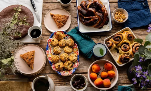 Assortiment gourmand de pâtisseries bio faites maison et café Marlette : gâteau au chocolat, muffins, pain aux raisins, fruits frais sur table en bois