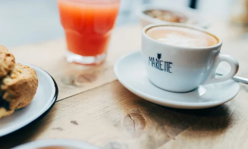 Tasse de café Marlette avec latte art, jus frais et viennoiserie sur table en bois