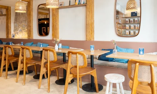 Intérieur chaleureux du coffee shop Marlette à Montmartre, avec chaises en bois, tables claires, banquettes bleues et luminaires design.